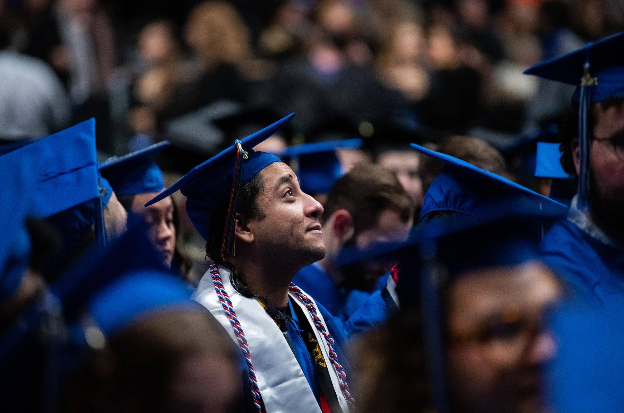 a GV graduate wearing a blue cap and gown smiles among the crowd of grads